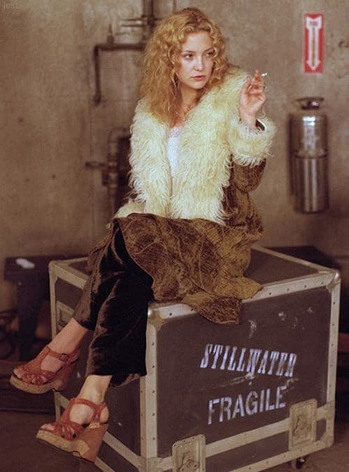 Penny Lane in Almost Famous wearing a faux fur trim jacket, smoking and sat on a box